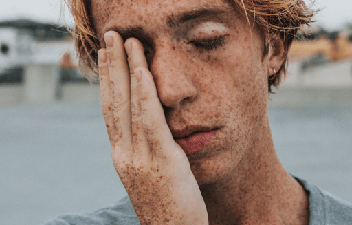 Person with freckles holding their hand over the right side of their face.