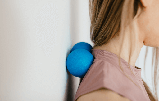 Person rolling lacrosse balls between their shoulders and a wall.